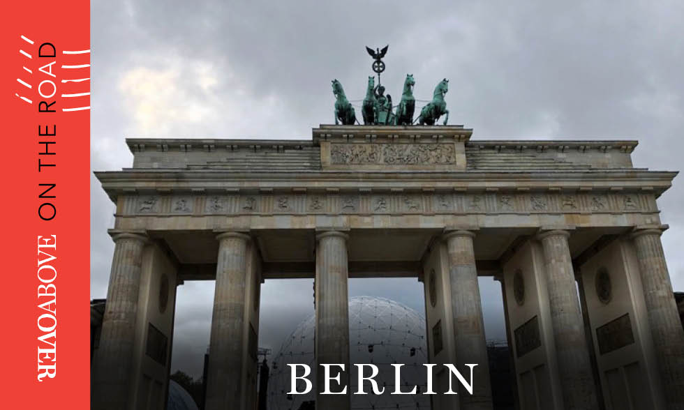 An image of Berlin’s Brandenburg Gate on a cloudy day with the words “Overabove On the Road” on the side
