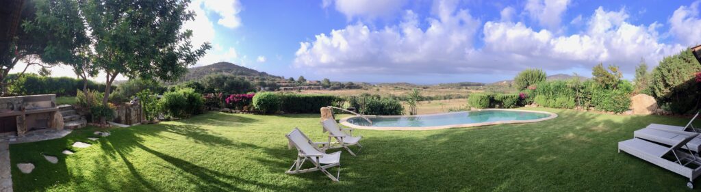 A panoramic view of a manicured lawn with white reclined chairs and a pool